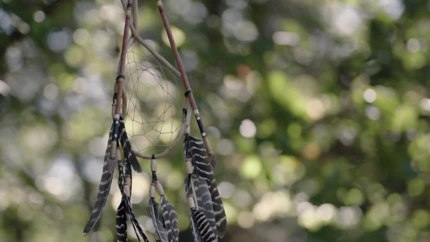 A dreamcatcher with feathers hangs on a sunny day