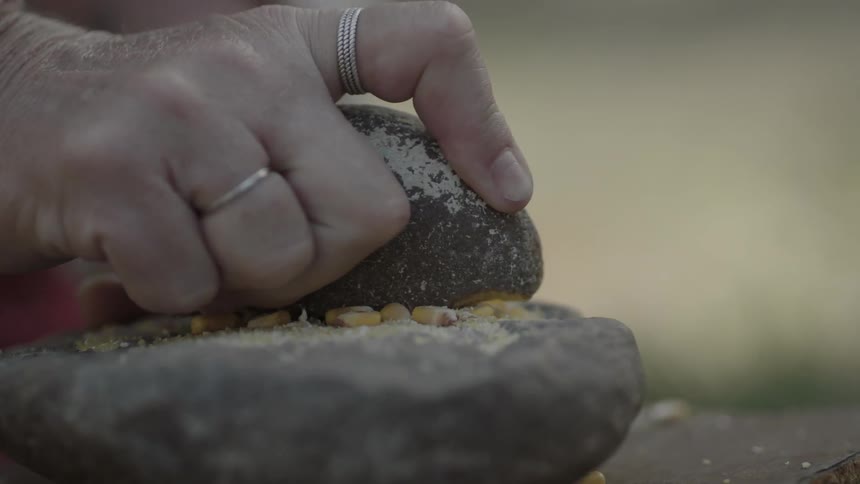 A person grinds corn on a stone slab
