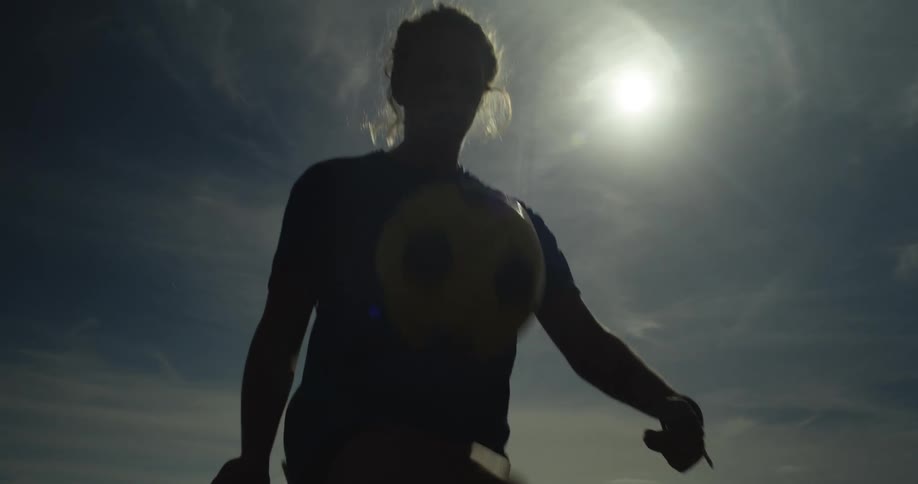 Sun shines behind the silhouette of a woman playing with a soccer ball