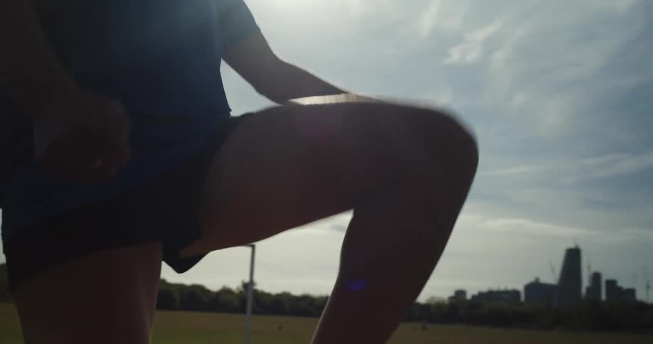 Sun shines behind the silhouette of a woman playing with a soccer ball