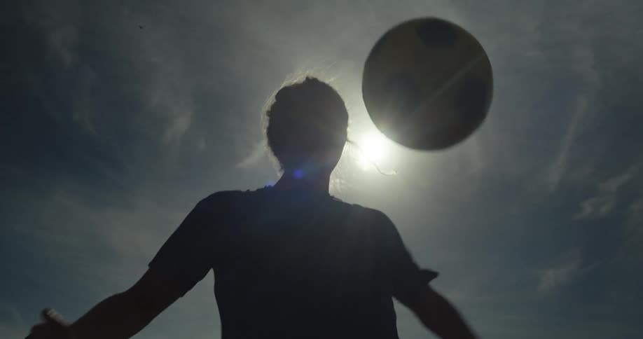 Silhouette of a woman practising with a soccer ball in a park