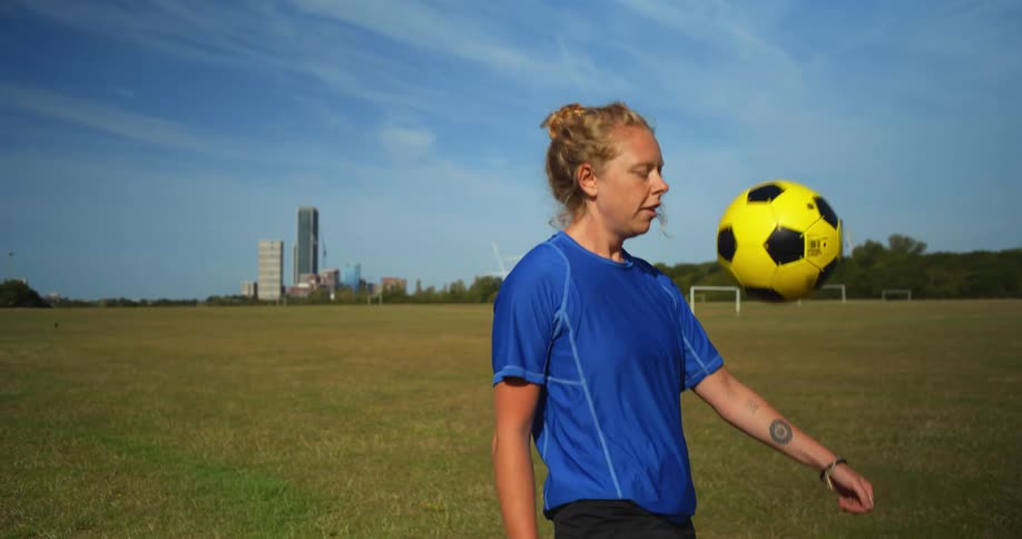 A young woman plays keep--ups with a soccer ball on a football pitch