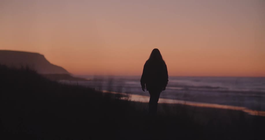 Silhouette of a woman walking towards the beach next to the ocean at sunset