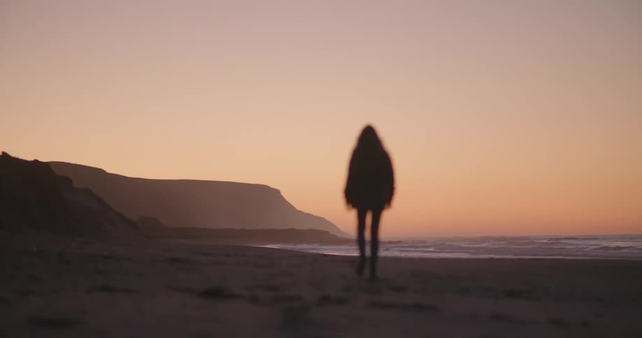 Woman walks along the beach silhouetted against the red sky