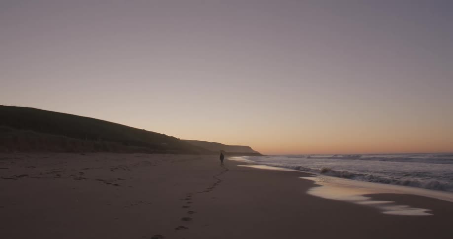Silhouette of a person leaving a trail of footsteps on the sand on the beach at sunset
