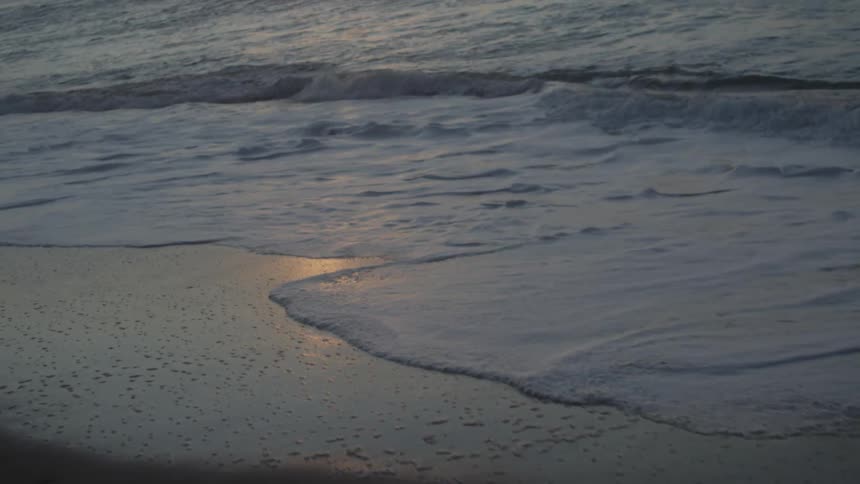Ocean waves washing ashore a sandy beach at sunset