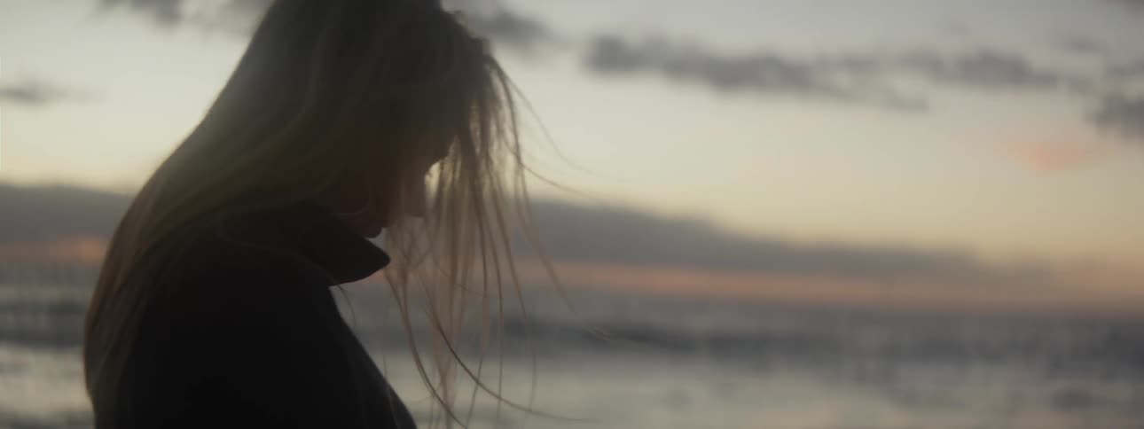 A teenage girl walking alone on a beach at dusk
