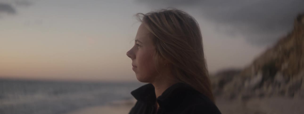 Close up of the face of a young woman standing on the beach looking at the horizon at evening