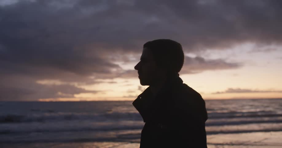 A man walks across a beach under a cloudy sky at sunset