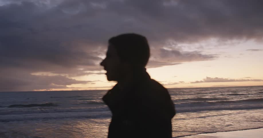 Silhouette of a woman walking on the beach next to the ocean at sunset