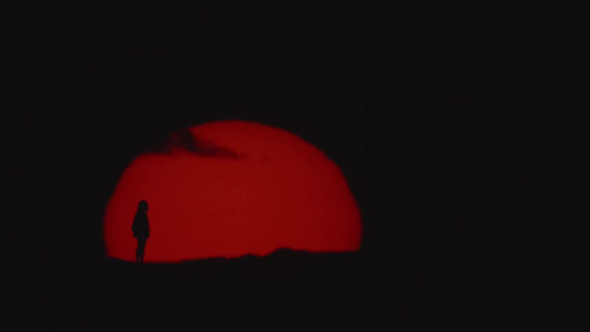 Silhouette of a woman standing in front of a giant red sun setting on the horizon