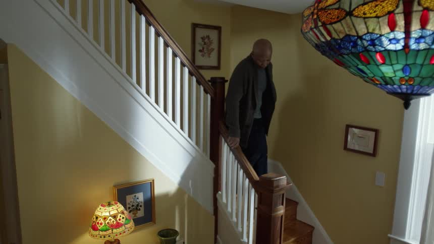 An older man walks slowly down the stairs looking sad