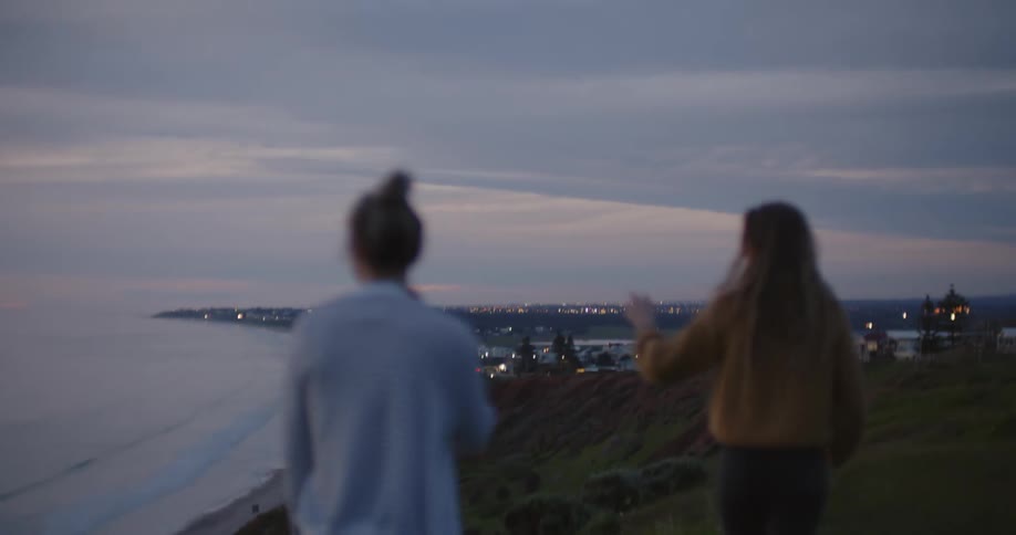 Two women walk on a hill by the beach