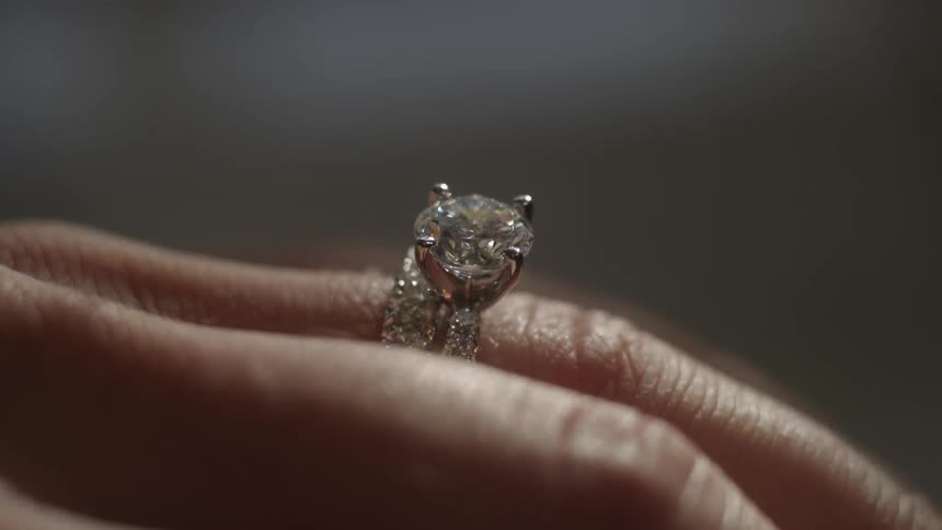 A large diamond ring is on the finger