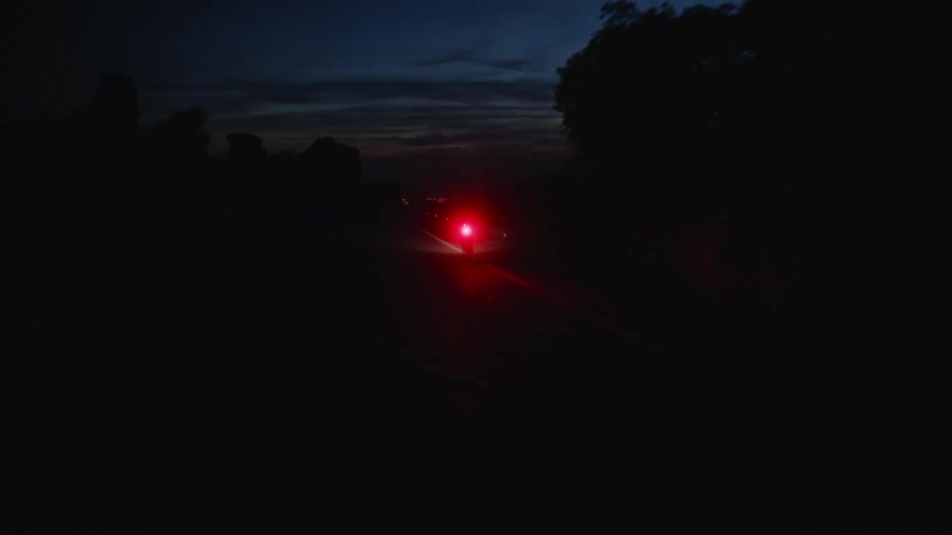 Cyclist rides bicycle with red flashing light on country road at night