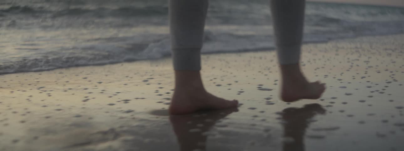 Bare feet walking on wet sand and surf at the beach at dusk