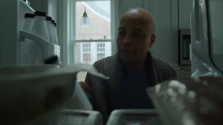 A person opens the doors of a fridge at home and takes a white bottle before closing them