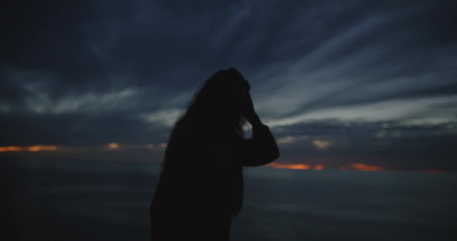 A woman walks on the beach at sunset
