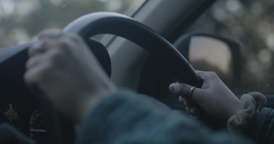 Close up of the hands of a woman on a steering wheel driving a car at morning