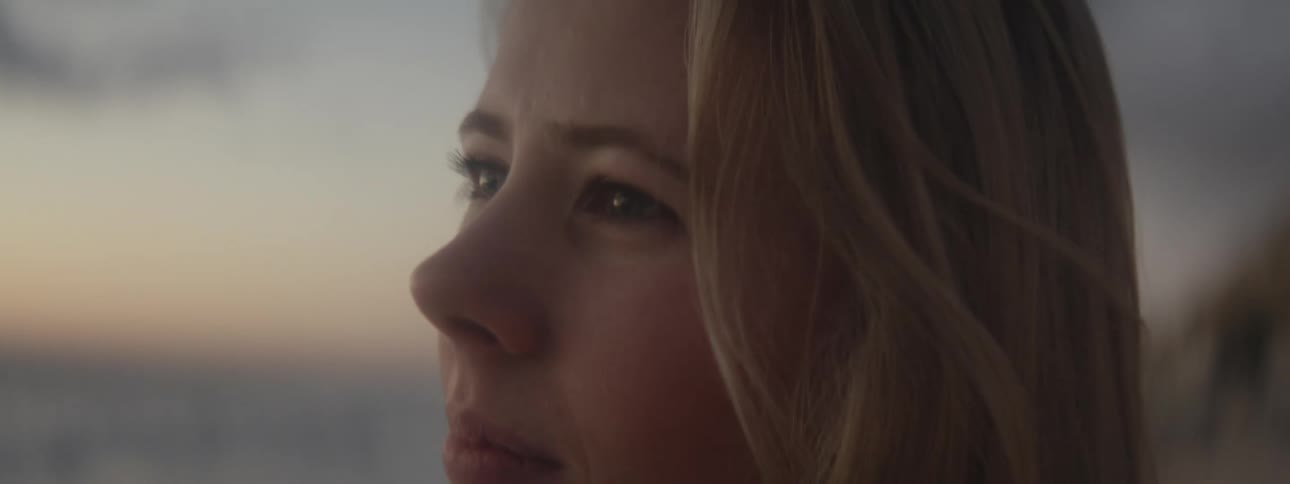 Close up of the face of a young woman standing on the beach looking at the horizon at evening
