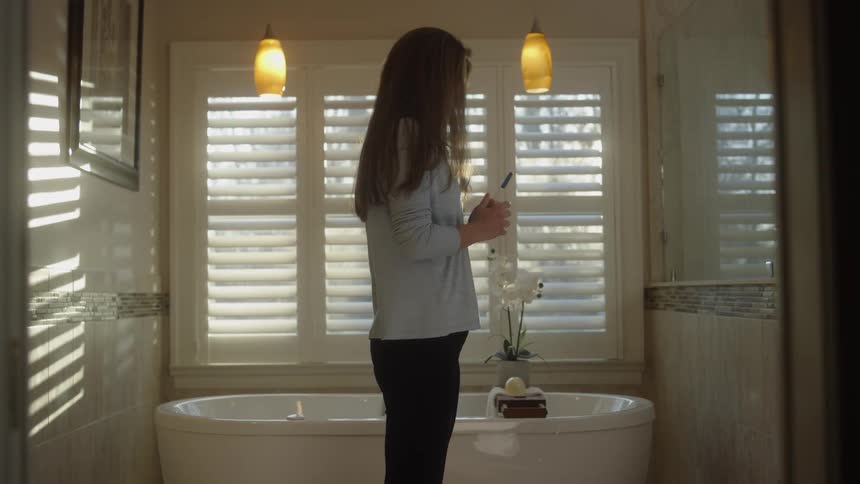 A woman is holding her pregnancy test as she paces across the bathroom