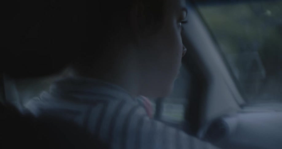 A teenage girl is looking through the windshield as she drives an automobile
