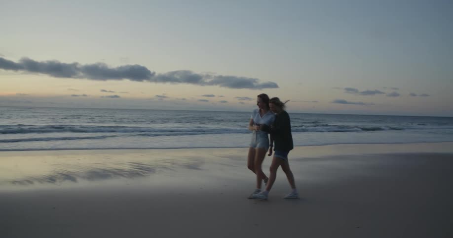 Young teenage women looking at pictures on a phone walking on the beach at evening