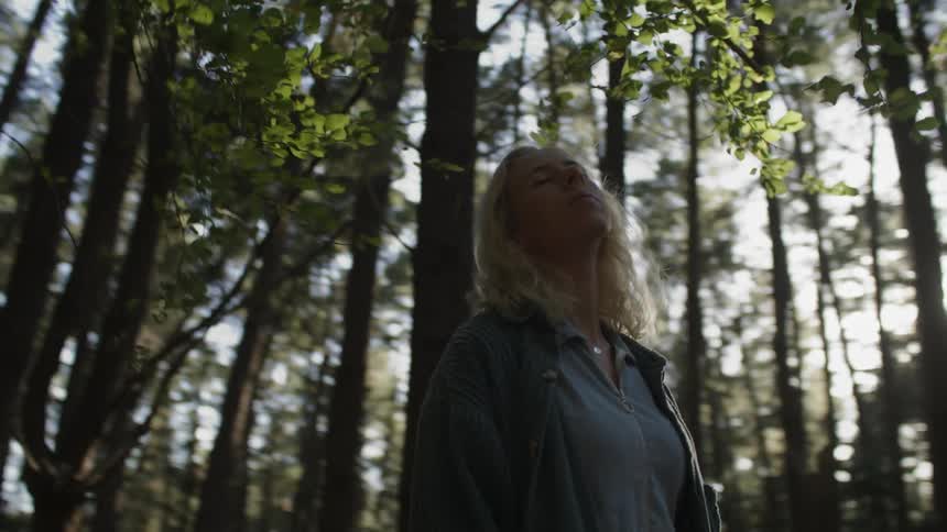 A woman standing in the woods with her head back and eyes closed