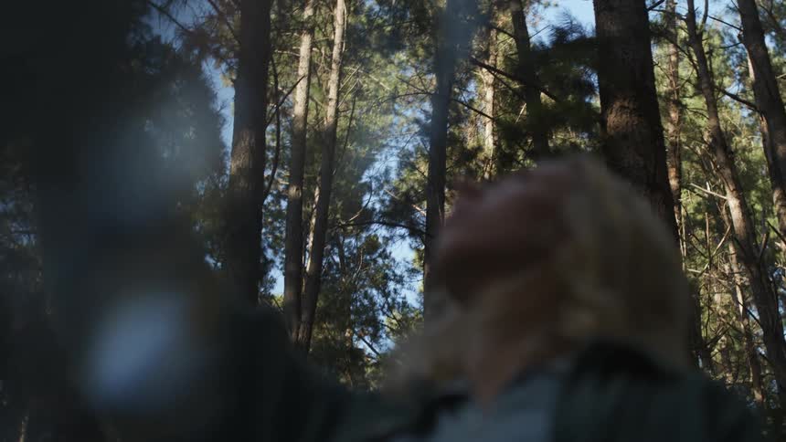 Blurred blonde woman wearing blue shirt and jacket looks up in the forest