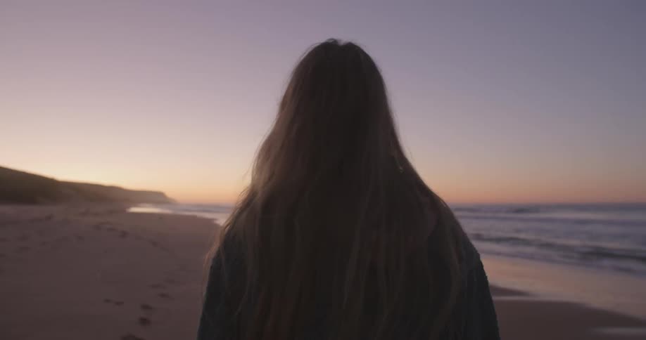 A woman walks along a sandy beach in the evening