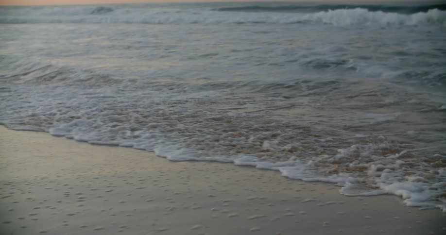 Ocean waves splash and foam as they come to a sandy shore at sunset