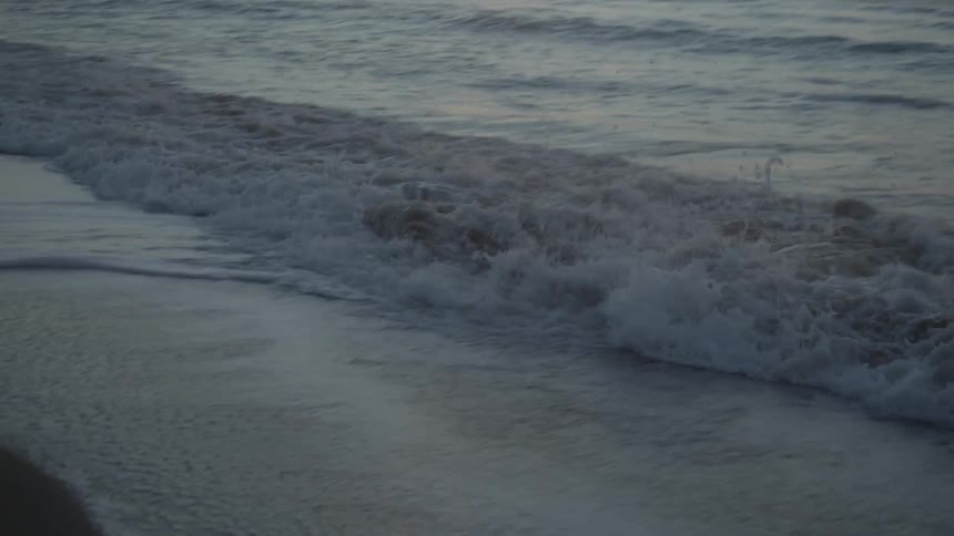 Waves crash onto beach foaming under a red sky