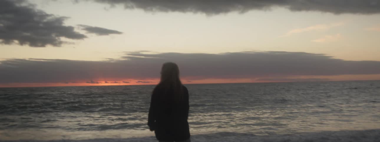 Woman walks along beach looking toward red tinted horizon