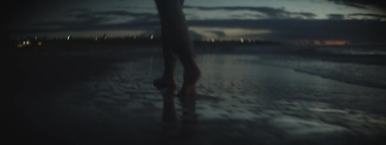 Following a barefoot woman walking on the wet sand on the coast of a beach at sunset