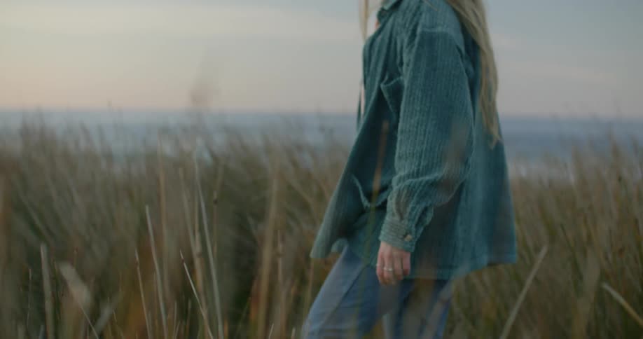 A woman walks in the tall grass by the beach