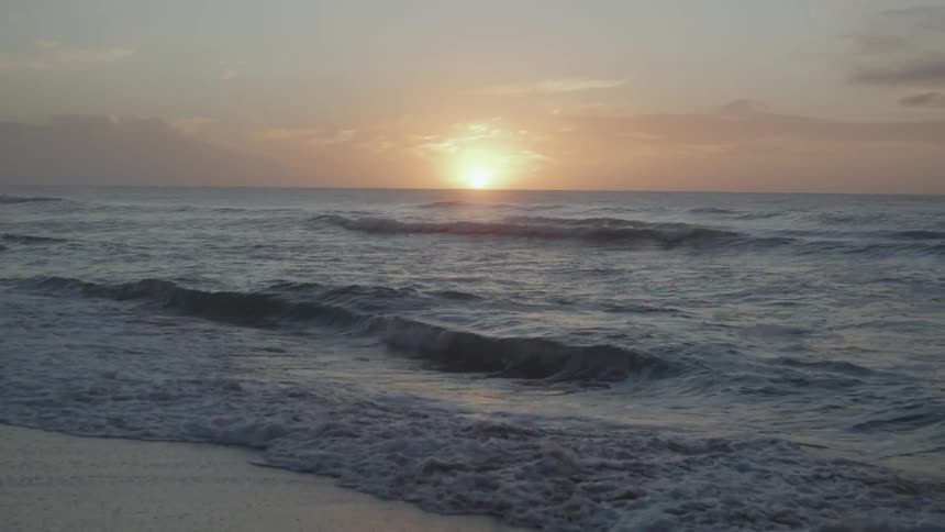 Sun shines on the horizon of the ocean seen from the coast of a beach at sunset