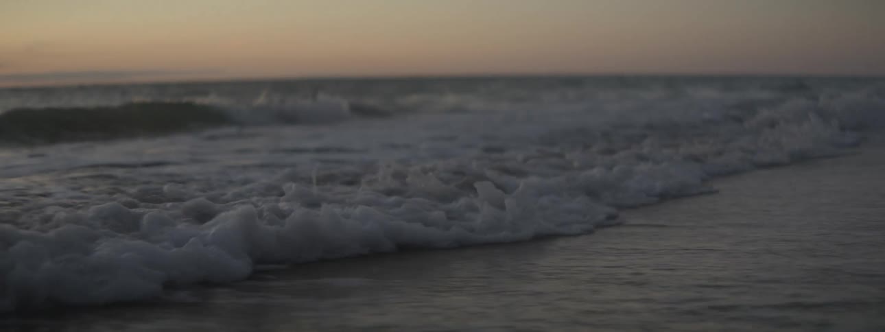 Small ocean waves gently crashing on the coast of a beach at sunset