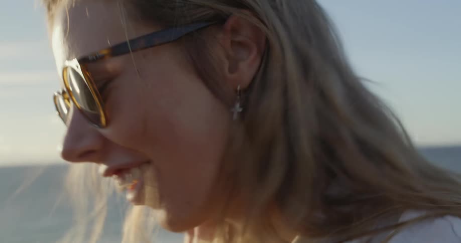 A woman standing on the beach smiling and nodding as the wind blows her hair