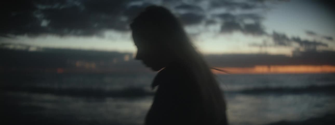 A woman with long blond hair is walking along the beach as the waves roll into shore