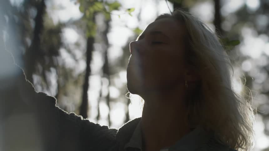 Close up of the face of a young woman looking up with eyes closed on the forest at morning