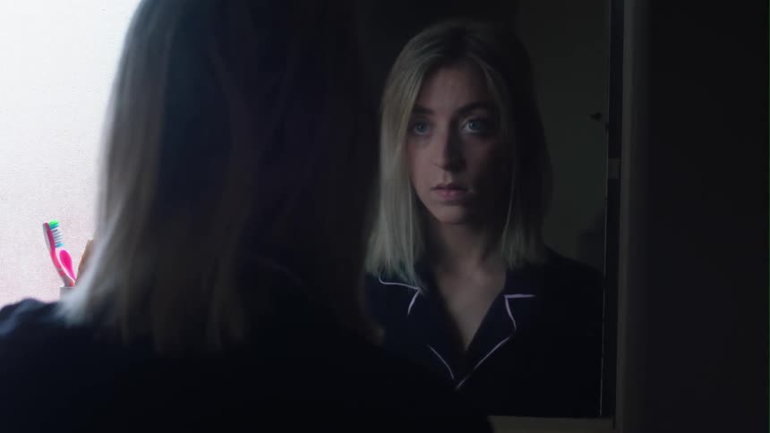 A woman is standing in her bathroom looking in the medicine cabinet and closes the door then looking into the mirror