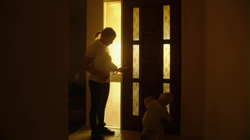 A woman reads a letter while her baby crawls by their front door