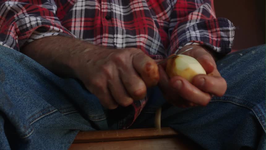 A man is sitting on a bench peeling a potato