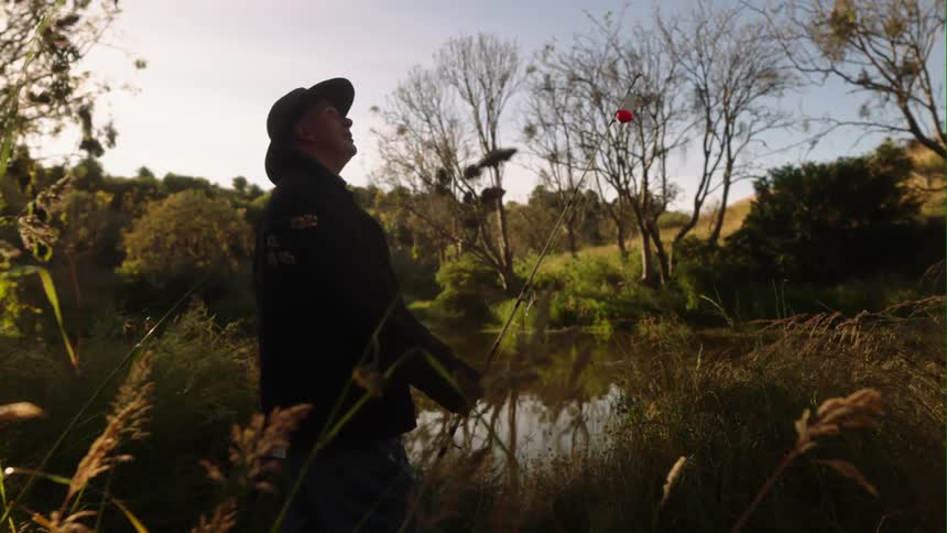 A man wearing a hat is standing outside near the water and looking up at the sky