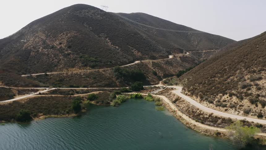 Aerial view of a road winding down the slopes of a mountain near a lake