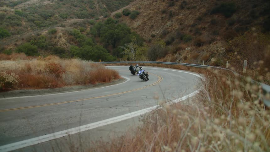 Two people drive motorcycles down a street