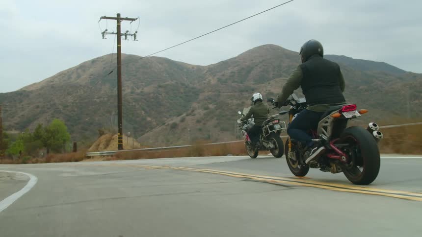Two people ride motorcycles on a road next to the mountains at daytime