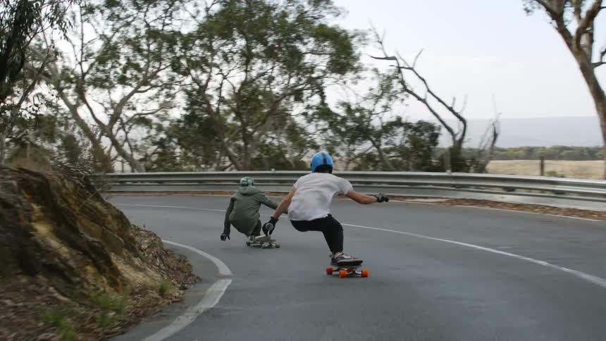 Two teenagers ride skateboards around a bend in the road
