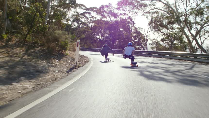 Two people skateboard down a street