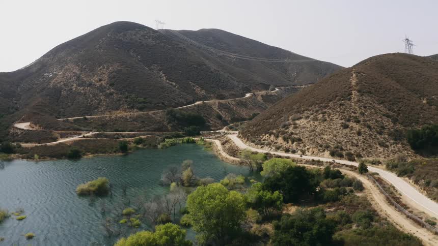 Roads wind along the side of mountains as two motorcycles pass by the lake in the valley